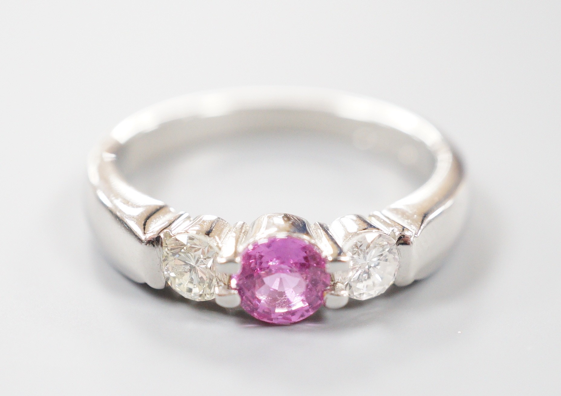 A modern platinum, single stone pink sapphire and two stone diamond set ring, size M/N, gross weight 6.5 grams